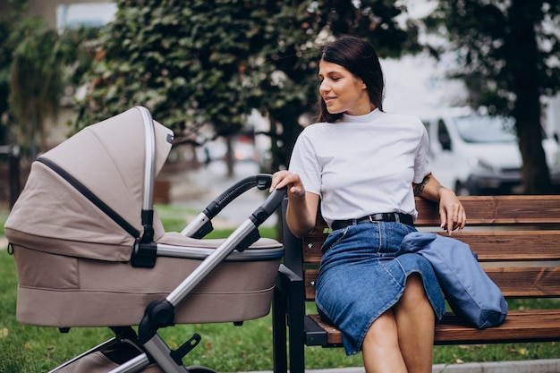 Young mother sitting on bench in park with baby stroller