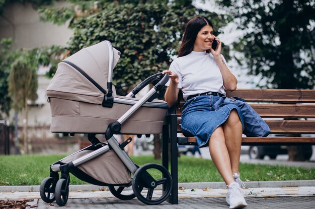 Young mother sitting on bench in park with baby stroller