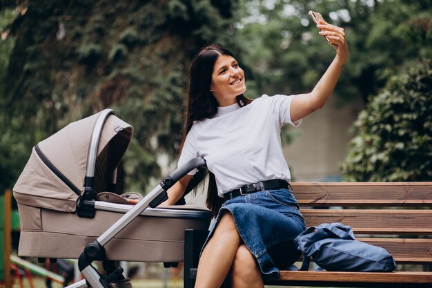 Young mother sitting on bench in park with baby stroller