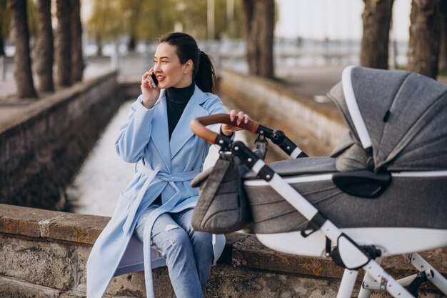 Молодая мать сидит с коляской в парке