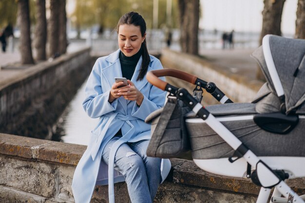 Young mother sitting with baby carriage in park