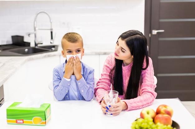 Young mother stay with her sick son in the kitchen and give tratments in the kitchen