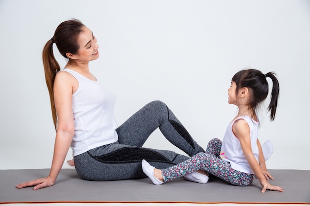 Young mother training lovely daughter with yoga