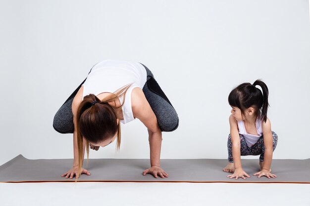 Young mother training lovely daughter with yoga