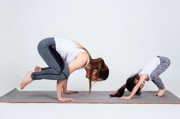 Young mother training lovely daughter with yoga