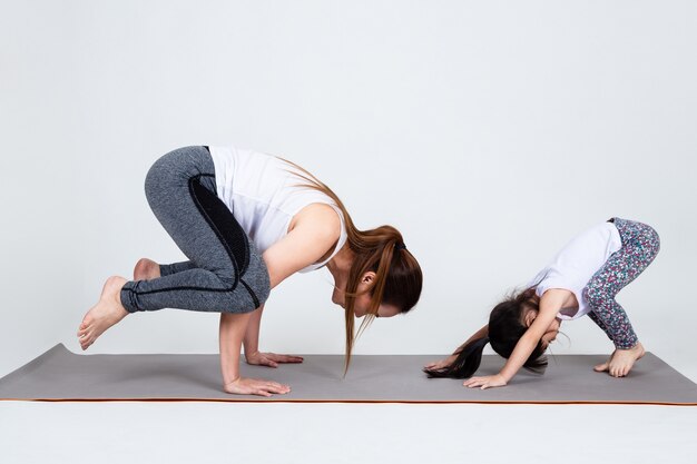 Young mother training lovely daughter with yoga