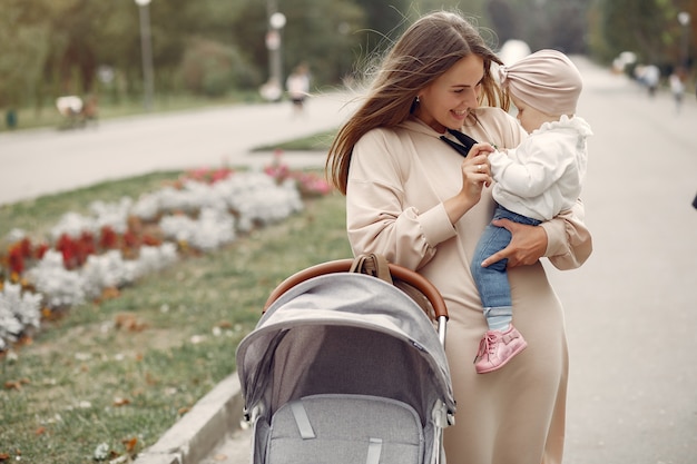 Foto gratuita giovane madre che cammina in un parco di autunno con il trasporto