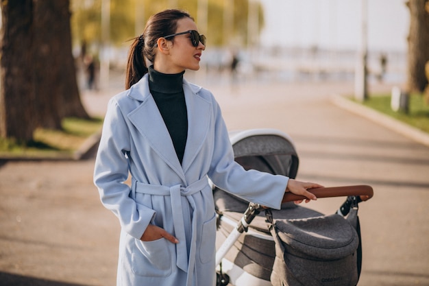 Foto gratuita giovane madre che cammina con carrozzina nel parco