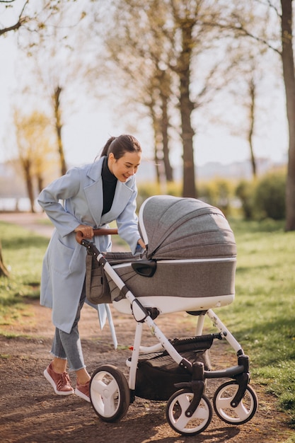 Foto gratuita giovane madre che cammina con carrozzina nel parco