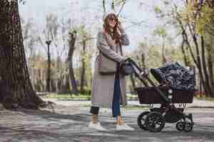 Foto gratuita giovane madre che cammina con carrozzina nel parco