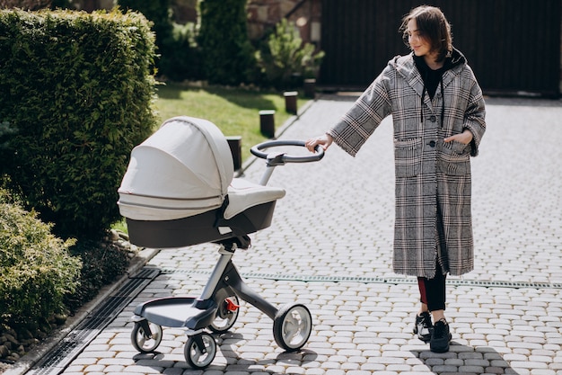 Foto gratuita giovane madre che cammina con la carrozzina in parco