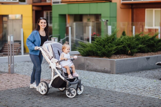 Free photo young mother walking with her baby and carries it in a beautiful pram. happiness.