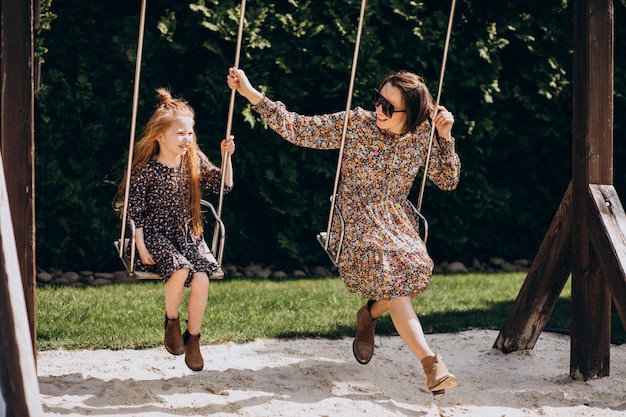 Young mother with daughter swinging in the backyard