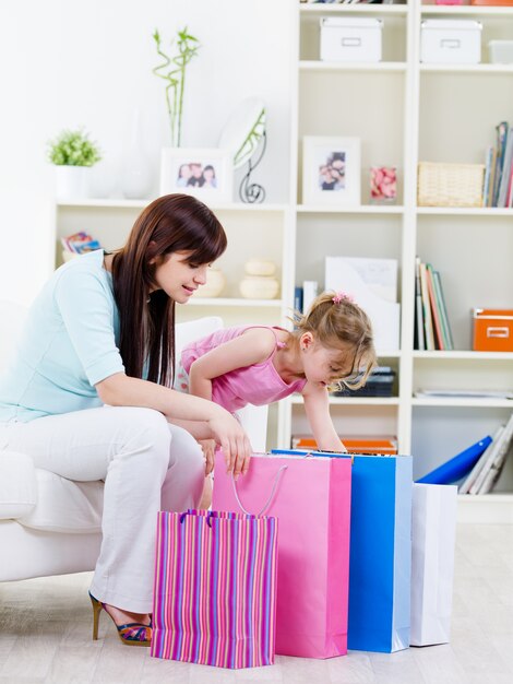 Young mother with little curiosity faughter opening purchase after shopping at home