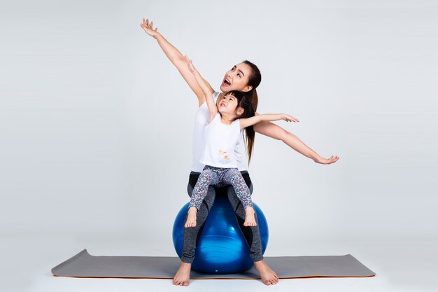 Young mother with little daughter exercise on fitness ball