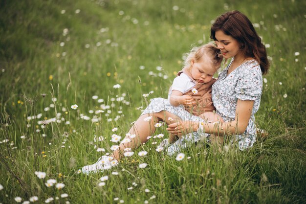 Молодая мать с маленькой дочерью в парке, сидя на траве