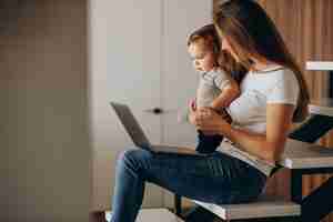 Foto gratuita giovane madre che lavora da casa sul computer portatile con il suo piccolo figlio