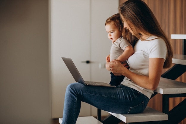 Young mother working from home on laptop with her little son