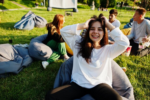 Young multi ethnic group of people watching movie at poof in open air cinema Close up portrait of funny girl