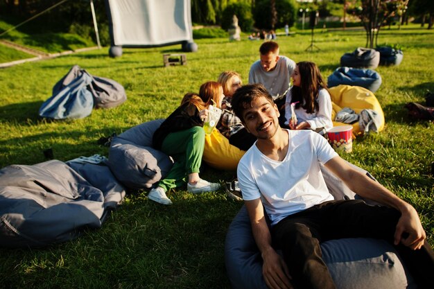 Young multi ethnic group of people watching movie at poof in open air cinema Close up portrait of funny guy