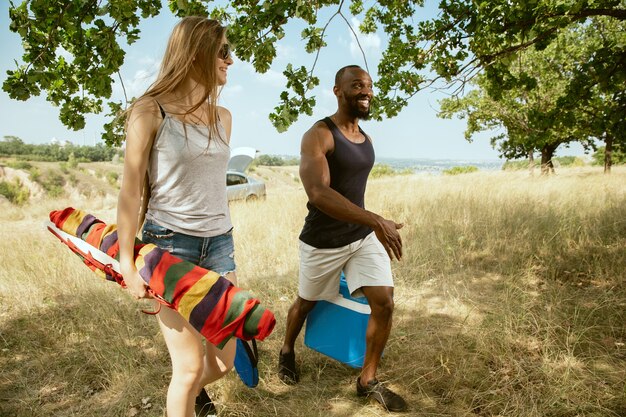 Young multiethnic international romantic couple outdoors at the meadow in sunny summer day. African-american man and caucasian woman having picnic together. Concept of relationship, summertime.