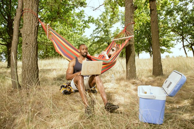 Young multiethnic international romantic couple outdoors at the meadow in sunny summer day. African-american man and caucasian woman having picnic together. Concept of relationship, summertime.