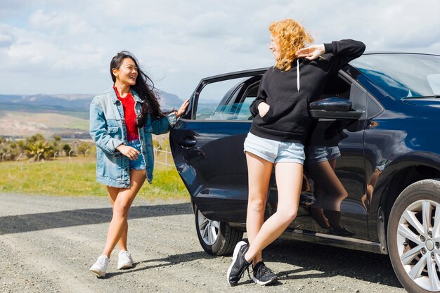 Young multiethnic women resting near car