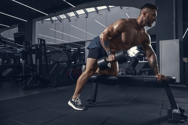 Young muscular athlete practicing in gym with the weights