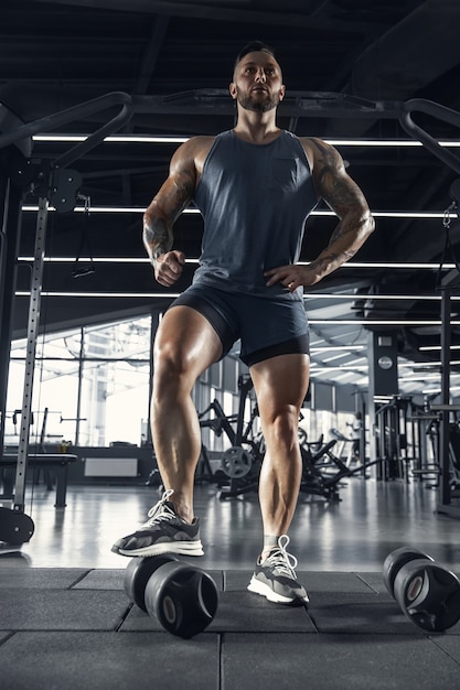 Бесплатное фото Молодой мускулистый спортсмен, тренирующийся в тренажерном зале, уверенно позирует с весами