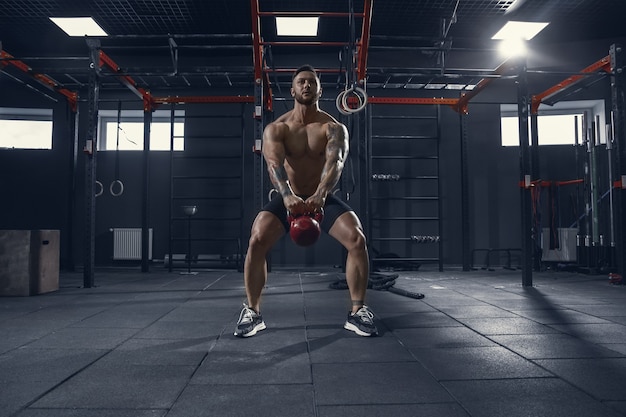 Young muscular athlete practicing squats in gym with the weight