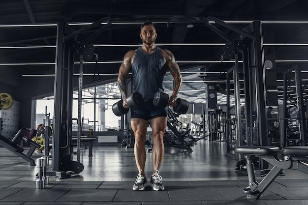 Young muscular caucasian athlete practicing in gym with the weights.