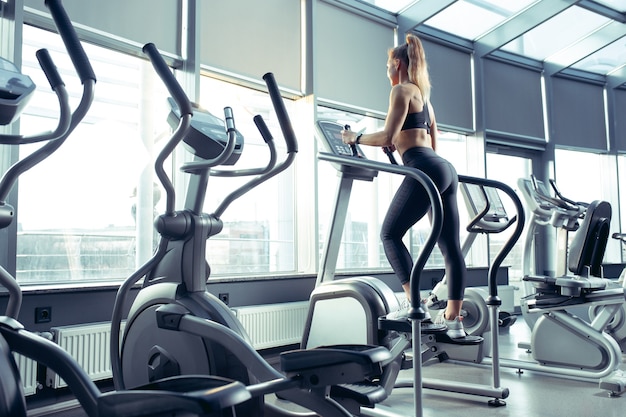 Молодая мускулистая кавказская женщина упражнениями в тренажерном зале, кардио. Спортивная (ый) женская модель делает силовые упражнения, тренируя верхнюю часть тела.