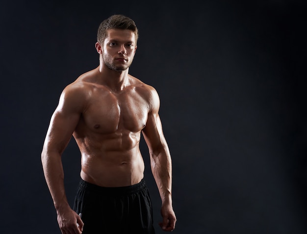 若い筋肉フィットスポーツマンが黒い背景に上半身裸でポーズ
