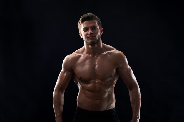 Young muscular fit sportsman posing shirtless on black backgroun