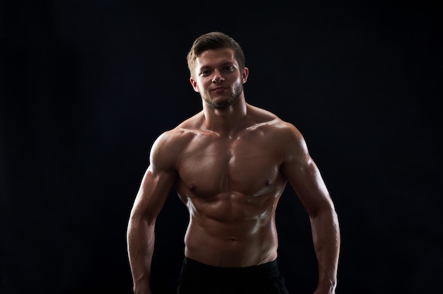 若い筋肉フィットスポーツマンが黒い背景に上半身裸でポーズ