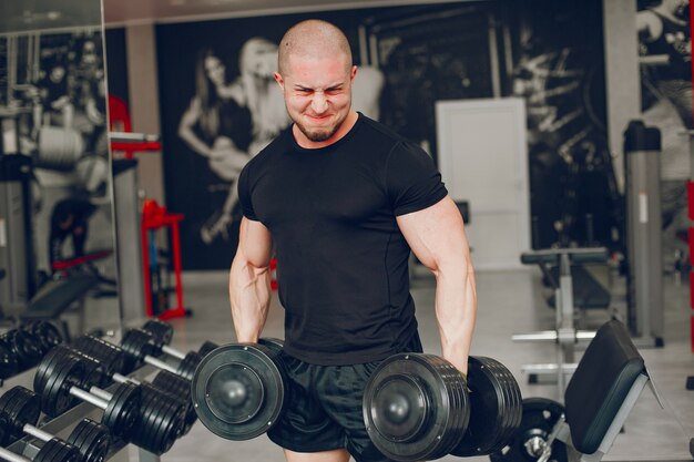 A young and muscular guy in a black t-shirt trains in a gym