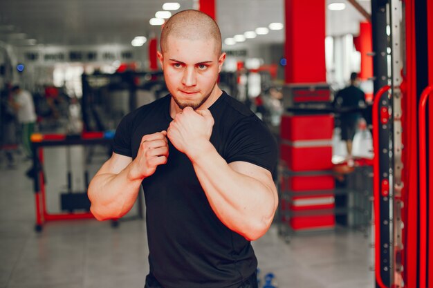 Молодой и мускулистый парень в черной футболке тренируется в тренажерном зале