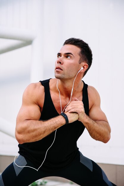 Young muscular guy preparing to workout, doing physical exercises, listening to music