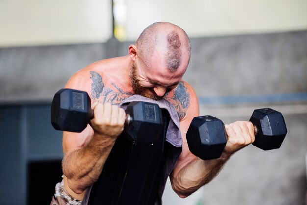 Молодой мускулистый татуированный сильный мускул бородатый европейец делает тяжелые упражнения