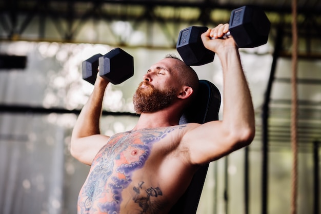 Young muscular tattooed strong muscle bearded european man doing hard exercise