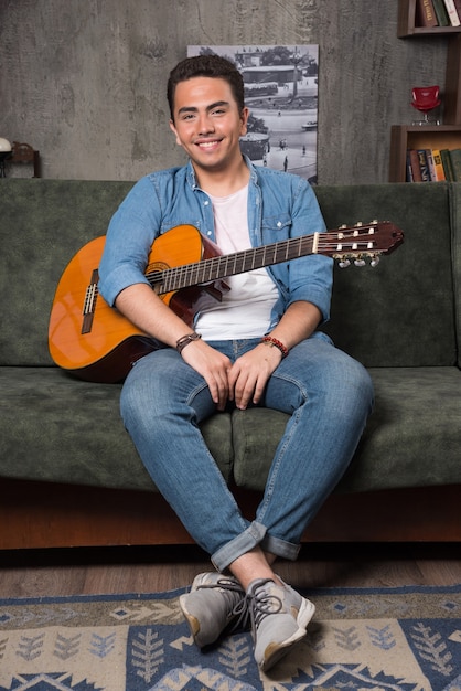 Young musician holding a beautiful guitar and sitting on sofa. High quality photo