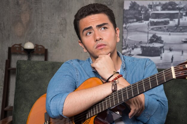 Young musician holding a beautiful guitar and sitting on sofa