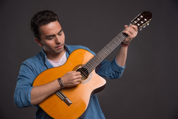 Young musician playing the guitar on black background