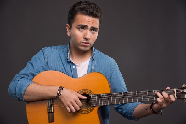 Young musician playing the guitar on black background