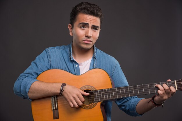 Young musician playing the guitar on black background