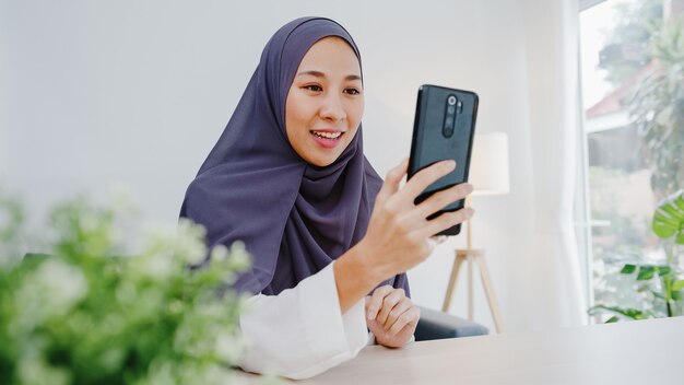 Young muslim businesswoman using smart phone talk to friend by videochat brainstorm online meeting while remotely work from home at living room.
