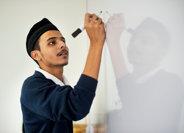 Foto gratuita il giovane uomo musulmano sta scrivendo un bordo bianco