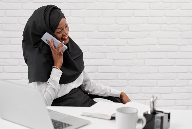 Young muslim woman in shirt and hijab talking by phone