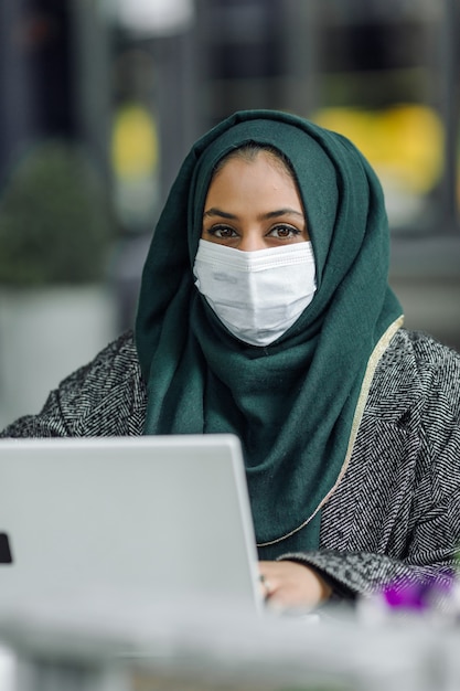 Young muslim woman sitting in a street cafe and looking in a laptop