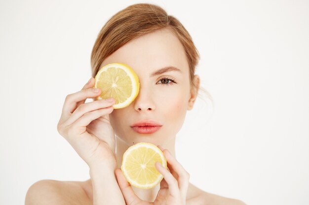 Young naked beautiful girl with clean healthy skin hiding eye behind lemon slice . Beauty spa cosmetology.